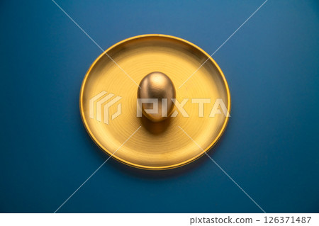 Golden easter egg placed on a golden plate on a blue background, representing luxury, celebration, and the festive spirit of easter, perfect for greeting cards or holiday promotions 126371487