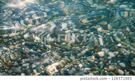 multi-colored stones under water on the sea, river. Natural background of stones, glare on the water 126371983