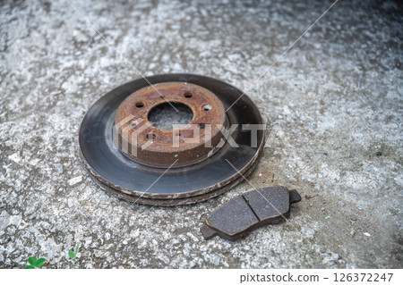 The old brake disc and brake pads are lying on a concrete surface, Repair of the car The old brake disc and brake pads are lying on a concrete surface, Repair of the car 126372247