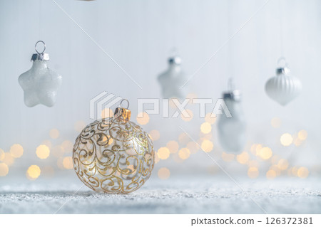 Golden christmas ball ornament resting on a snow-dusted surface, surrounded by hanging star and teardrop ornaments, creating a festive scene with warm bokeh lights Golden christmas ball ornament resting on a snow-dusted surface, surrounded by hanging star and teardrop ornaments, creating a festive scene with warm bokeh lights 126372381
