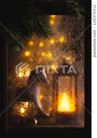 Christmas lights illuminating a rocking horse toy and a lantern behind a frozen window with visible ice crystals, creating a cozy and festive scene 126372412