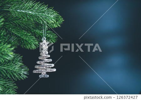 Silver spiral christmas tree ornament hanging from a green branch on dark background, creating a festive and magical atmosphere with copy space 126372427