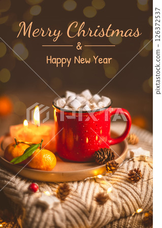 Christmas greeting card with a red mug full of hot chocolate with marshmallows, tangerines, a lit candle, pine cones, cookies and string lights, resting on a warm knitted sweater Christmas greeting card with a red mug full of hot chocolate with marshmallows, tangerines, a lit candle, pine cones, cookies and string lights, resting on a warm knitted sweater 126372537