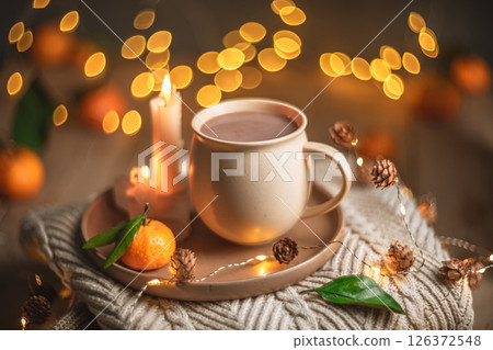 Christmas hot chocolate with tangerines and burning candles on a stack of knitted sweaters creates a cozy winter atmosphere with warm bokeh lights Christmas hot chocolate with tangerines and burning candles on a stack of knitted sweaters creates a cozy winter atmosphere with warm bokeh lights 126372548