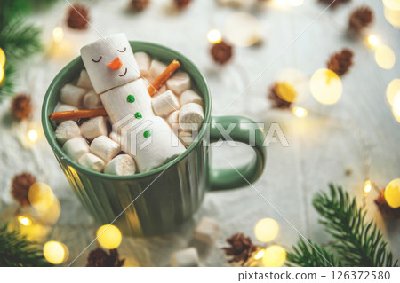 cute christmas card, Cheerful marshmallow snowman relaxes in a green mug of hot chocolate, surrounded by mini marshmallows, cinnamon sticks, and festive christmas lights, creating cozy holiday scene 126372580