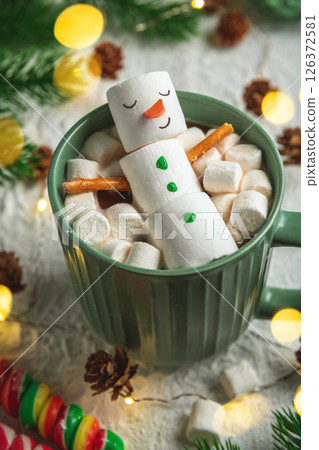 cute christmas card, Cheerful marshmallow snowman relaxes in a green mug of hot chocolate, surrounded by mini marshmallows, cinnamon sticks, and festive christmas lights, creating cozy holiday scene cute christmas card, Cheerful marshmallow snowman relaxes in a green mug of hot chocolate, surrounded by mini marshmallows, cinnamon sticks, and festive christmas lights, creating cozy holiday scene 126372581