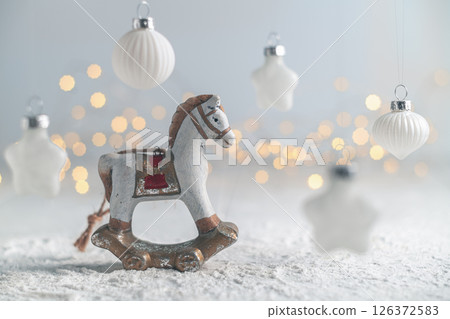 Charming christmas scene featuring a vintage rocking horse ornament on a snow-covered surface, surrounded by twinkling lights and hanging white star and ball ornaments 126372583