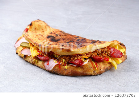 Folded Pizza Sandwich Panuozzo with Ham, Sausage, Cheese and Pickles on Stone Surface Folded Pizza Sandwich Panuozzo with Ham, Sausage, Cheese and Pickles on Stone Surface 126372702