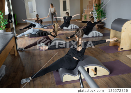 Woman doing mermaid exercise on back spine corrector. Reformer pilates studio machine for fitness workouts in gym. Fit, healthy and strong authentical body. Fitness concept. 126372856