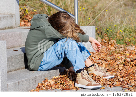 Young upset depressed teen kid boy sits alone on urban steps hands covering face in despair. Distressed hidden expression anxiety, sadness, emotional breakdown isolation insecurity, mental health Young upset depressed teen kid boy sits alone on urban steps hands covering face in despair. Distressed hidden expression anxiety, sadness, emotional breakdown isolation insecurity, mental health 126372981