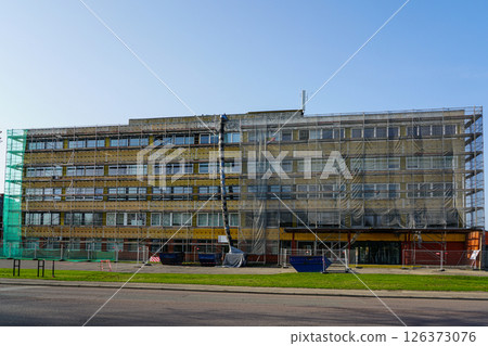 Renovation of office building covered in scaffolding and protective net during reconstruction work Renovation of office building covered in scaffolding and protective net during reconstruction work 126373076