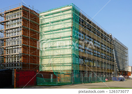 Renovation of office building covered in scaffolding and protective net during reconstruction work 126373077