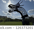 Silhouetted Metal Dragon Sculpture Against Bright Sky 126373201