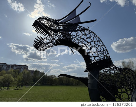 Silhouetted Metal Dragon Sculpture Against Bright Sky 126373201