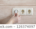 Woman Plugging Power Plug. Electrical plug in outlet socket at home. 126374097