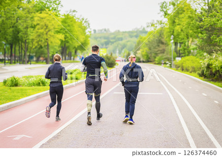 Three active runners move along shared running path in vibrant spring park. Fitness, sport, friendship, group activity, team training, lifestyle concept Three active runners move along shared running path in vibrant spring park. Fitness, sport, friendship, group activity, team training, lifestyle concept 126374460
