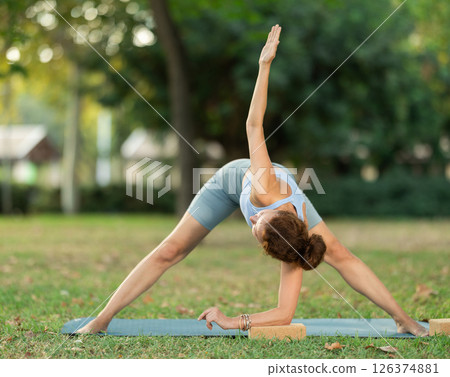 Fitness, sport and healthy lifestyle concept: woman doing yoga pose - vrikshasana pose on mat in park 126374881