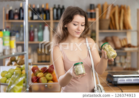 Young girl is choosing pickled mushrooms in grocery store 126374913