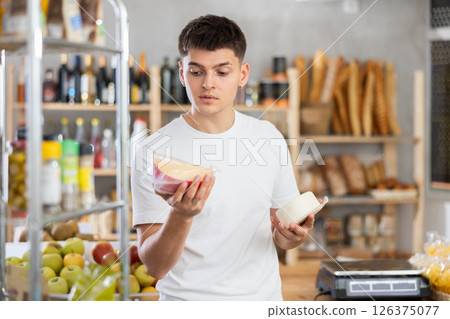 Guy carefully chooses tasty cheese in grocery store Guy carefully chooses tasty cheese in grocery store 126375077