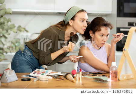 Two female friends applying makeup by vanity mirror at home Two female friends applying makeup by vanity mirror at home 126375092