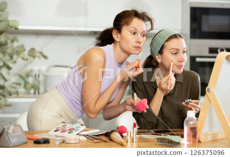 Two female friends applying makeup by vanity mirror at home 126375096