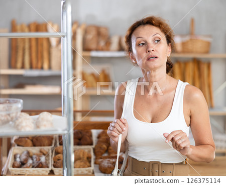 Young European woman near window of bakery food court store examines assortment 126375114