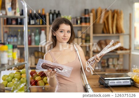 Young woman chooses dried sausage in store Young woman chooses dried sausage in store 126375126