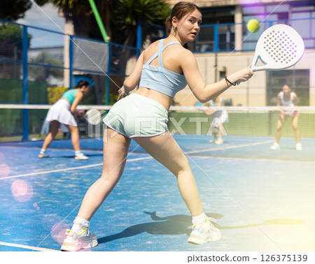 Woman actively playing paddle tennis on a court in a park against the background of glare 126375139