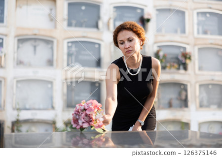 Sorrowful woman puts bouquet of hydrangeas on grave of deceased friend, mourns loss Sorrowful woman puts bouquet of hydrangeas on grave of deceased friend, mourns loss 126375146