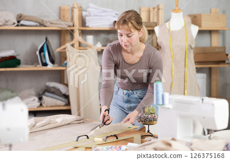 Female dressmaker using fabric shears to cut linen in workshop 126375168