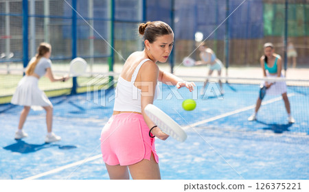 Young woman playing paddle tennis against team of women 126375221