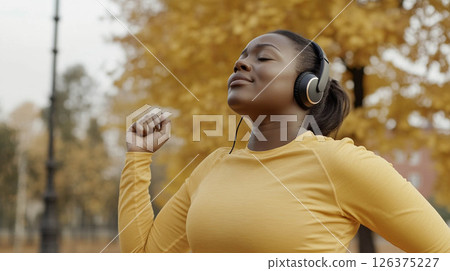 Tired African woman running outdoors in a city park on a crisp autumn morning with headphones on. Generated image 126375227