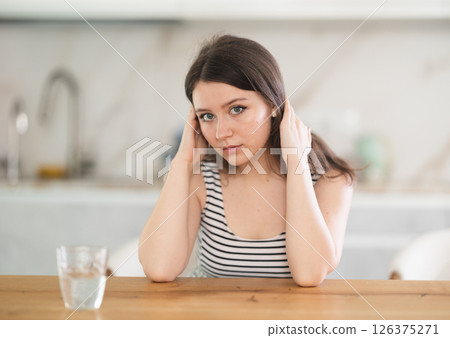Thoughtful young woman sitting at table Thoughtful young woman sitting at table 126375271