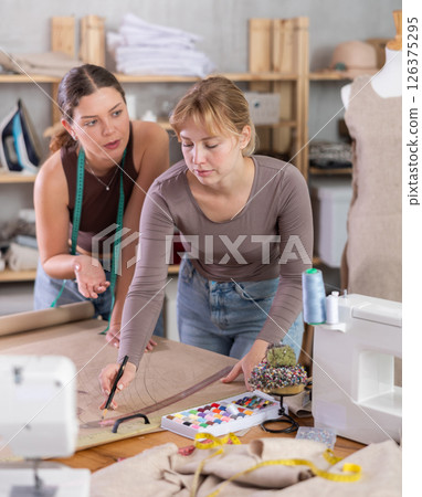 Female seamstresses drafting new clothing pattern on paper in sewing workshop Female seamstresses drafting new clothing pattern on paper in sewing workshop 126375295