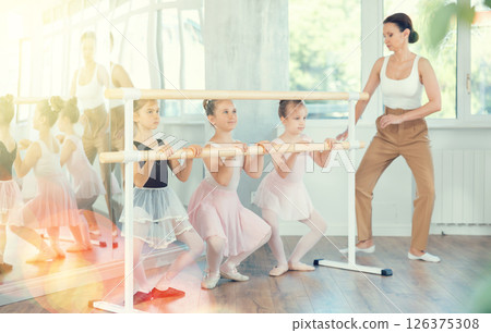 Woman teacher corrects girls in plie movement 126375308