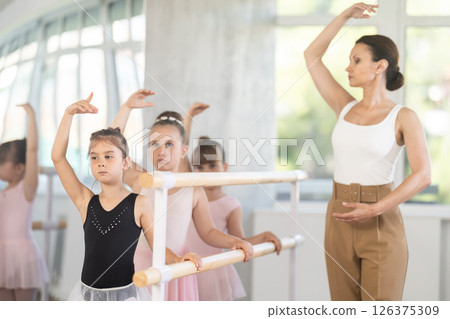 Little ballerinas learn to get into fourth position in ballet class. Choreographer helps them with this 126375309