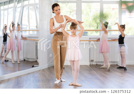 In studio, mentor corrects girls arm and leg, teaches correct dynamics and execution of movements In studio, mentor corrects girls arm and leg, teaches correct dynamics and execution of movements 126375312