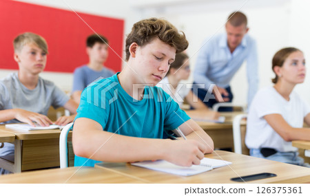 Diligent teenage student making notes of teacher lecture 126375361