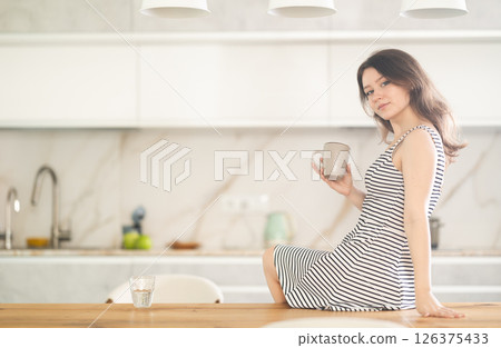 Young woman with cup sitting on table Young woman with cup sitting on table 126375433