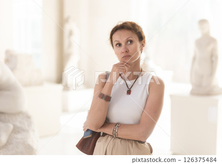Portrait of woman visitor with smartphone in hands looking exhibition of statues in museum 126375484