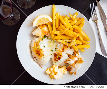 fried cuttlefish drizzled with white garlic and parsley sauce,lemon wedge and french fries on plate 126375581