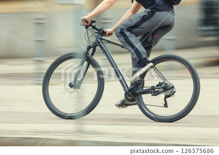 Man in sport suit riding fast black bicycle on European city street dynamic motion blurred background on sunny day. Urban bike commute work ride employee healthy lifestyle eco-friendly transport 126375686