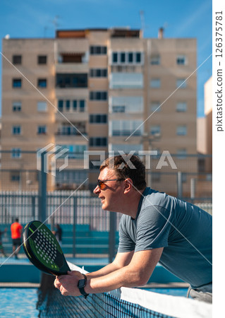 Man enjoying a sunny day of padel tennis on an outdoor court. 126375781