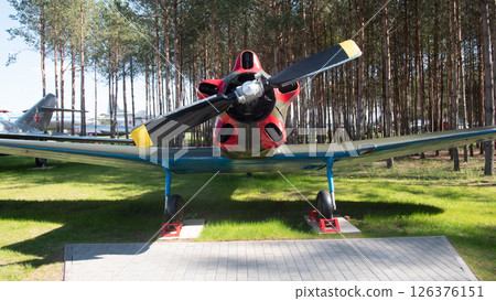 A vintage Soviet aircraft stands proudly in a serene park, surrounded by tall trees and grass, representing the rich aviation history of the USSR. A vintage Soviet aircraft stands proudly in a serene park, surrounded by tall trees and grass, representing the rich aviation history of the USSR. 126376151