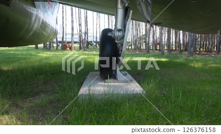 An aircraft landing gear is prominently displayed on a concrete base surrounded by tall trees in a serene forest setting, reflecting historical aviation advancements. An aircraft landing gear is prominently displayed on a concrete base surrounded by tall trees in a serene forest setting, reflecting historical aviation advancements. 126376158