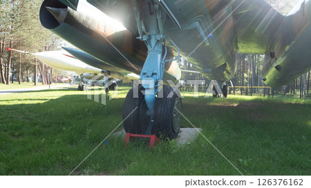 Soviet aircraft is showcased in an outdoor exhibition, with strong emphasis on the landing gear amidst lush greenery and surrounding trees, evoking a sense of history. Soviet aircraft is showcased in an outdoor exhibition, with strong emphasis on the landing gear amidst lush greenery and surrounding trees, evoking a sense of history. 126376162
