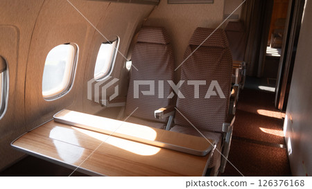 Seating area of a vintage USSR airplane highlights two plush seats and a wooden table, reflecting the unique design and atmosphere of air travel in a past era. 126376168