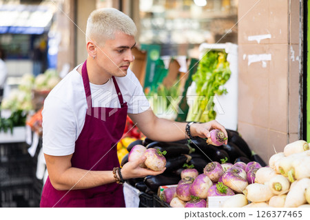Grocery store employee places ripe radish on a display case at street store 126377465