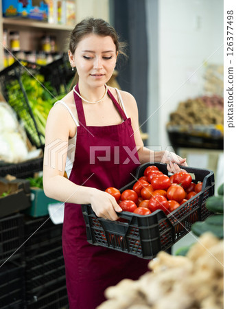 Female seller holding a container of tomatoes in a supermarket Female seller holding a container of tomatoes in a supermarket 126377498