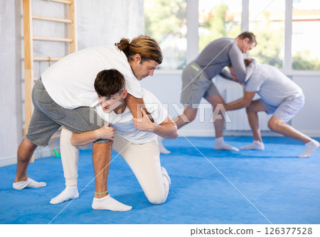 Man ang guy practicing judo techniques in gym with sparring partner, in background men are sparring 126377528
